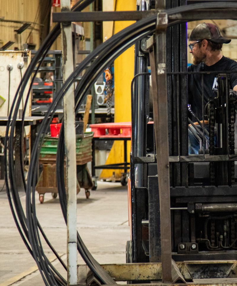 M3 employee drives a forklift of rolled metal tubing