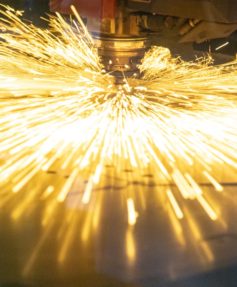 Laser cutter throwing sparks as it cuts through piece of metal